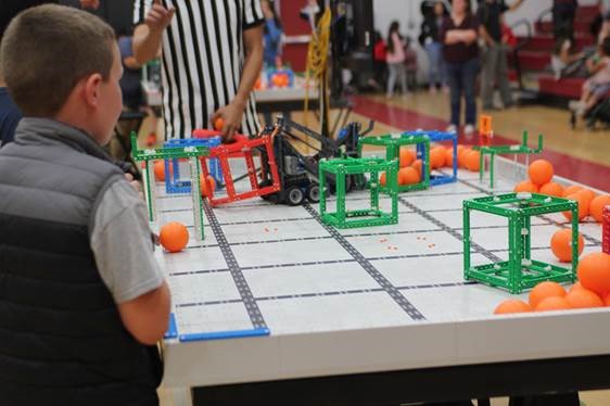 Student testing robot on table, the robot is surrounded by different placed obstacles along with ping-pong balls. 