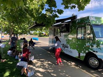 Kids sitting down during a lesson outside of the Mobile Teaching Kitchen.